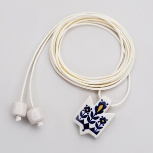 Handmade ceramic Tryzub pendant necklace with floral folk art design in navy blue and yellow on a white base, featuring an adjustable cream cord with ceramic bead ends.