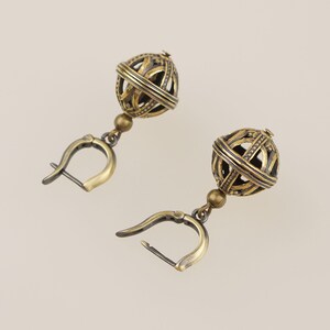 May include: A pair of antique brass earrings. Each earring features a spherical cage design with intricate detailing, suspended from a hinged clasp. The earrings have a vintage aesthetic, with a warm, aged brass finish.