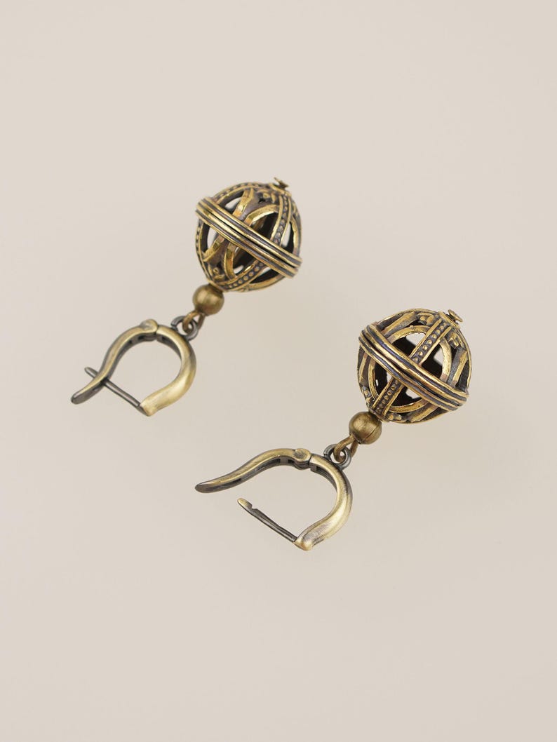 May include: A pair of antique brass earrings. Each earring features a spherical cage design with intricate detailing, suspended from a hinged clasp. The earrings have a vintage aesthetic, with a warm, aged brass finish.