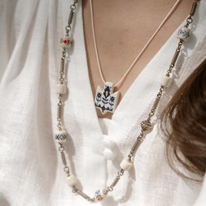 Handmade ceramic wrap necklace featuring a hand-painted Ukrainian Trident pendant with traditional folk flower design in blue.