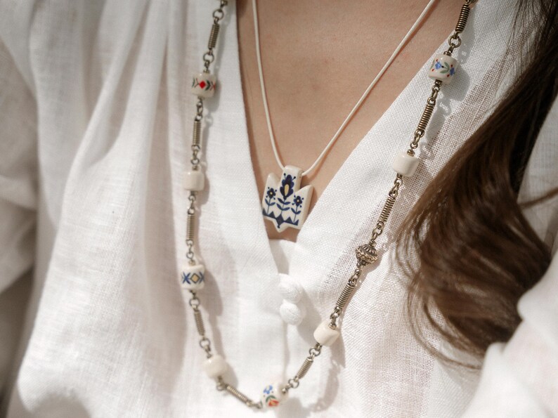 Handmade ceramic wrap necklace featuring a hand-painted Ukrainian Trident pendant with traditional folk flower design in blue.