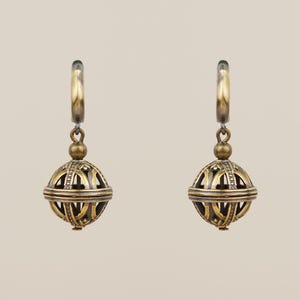 May include: A pair of antique gold-colored earrings. Each earring features a hoop, a small ball, and a larger, openwork sphere with intricate geometric patterns. The earrings are suspended against a neutral background.