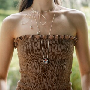 Handmade ceramic wrap necklace featuring a hand-painted Ukrainian Trident pendant with traditional folk flower design in red, blue, green and yellow.