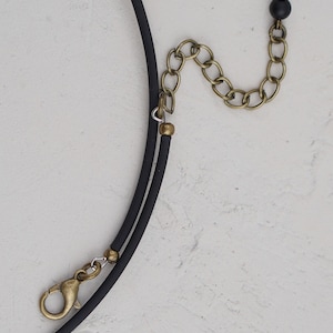 May include: A black choker necklace with a gold chain extender and a small black bead. The necklace is made of a soft, flexible material.
