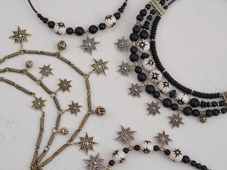 May include: A set of three necklaces featuring black and white beads with star-shaped charms. The necklaces are made of different materials, including metal, wood, and plastic.