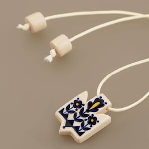 Unique Ukrainian Tryzub pendant necklace featuring a folk art floral design where navy is the dominant color, hand-painted on a cream ceramic base with an adjustable wrap cord.