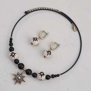 May include: A black choker necklace with white and black star-shaped beads and a large star pendant. The necklace is paired with matching earrings with white and black star-shaped beads.