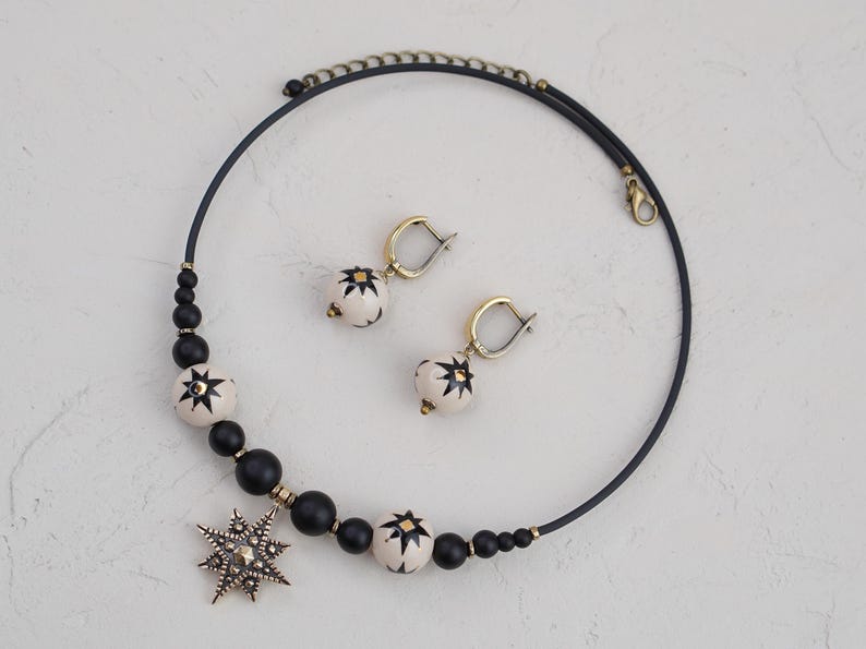 May include: A black choker necklace with white and black star-shaped beads and a large star pendant. The necklace is paired with matching earrings with white and black star-shaped beads.