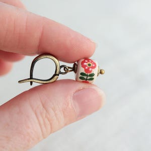 May include: A white ceramic bead earring with a red floral design and a gold-toned hook.