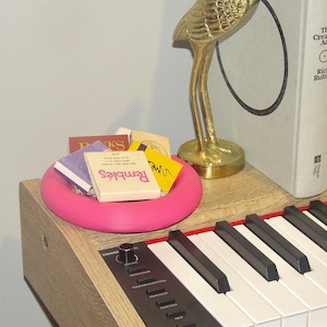 May include: A pink ring-shaped dish with a variety of matchbooks inside, including "Reminisce" and "Books". The dish is sitting on top of a wooden keyboard with black and white keys.
