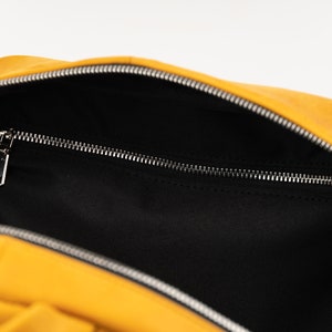 Puede incluir: Una mochila amarilla con forro negro y un bolsillo con cremallera. La mochila est&aacute; abierta y el forro es visible.