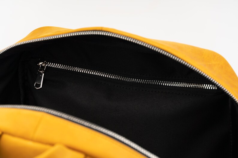 Puede incluir: Una mochila amarilla con forro negro y un bolsillo con cremallera. La mochila est&aacute; abierta y el forro es visible.