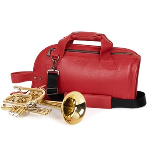 May include: A red leather trumpet case with a black strap and a gold trumpet. The case has a zipper closure and a handle.