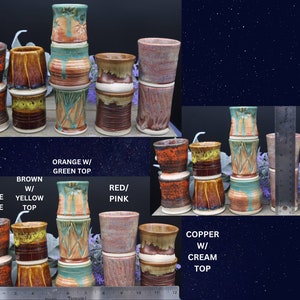 May include: A collection of handmade ceramic mugs in various colors and patterns, including orange with green top, brown with yellow top, orange with blue top, red/pink, and copper with cream top. The mugs are stacked in groups of three, with a ruler in the background for size reference.