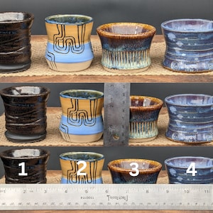 May include: Set of six small ceramic cups with various glaze patterns. The cups are arranged in three rows of two. The cups are all different colors, including blue, brown, and yellow. The cups are all about 3 inches tall.