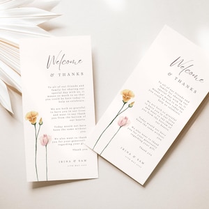 May include: Two ivory wedding welcome cards with floral illustrations. The cards feature the text "Welcome & Thanks" in elegant script, along with a personalized message and the names "Irina & Sam". Delicate watercolor flowers in shades of yellow and pink adorn the cards.