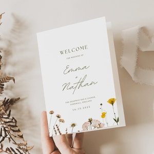 May include: A white wedding order of service with a floral design featuring yellow and pink flowers. The text reads "Welcome, The Wedding of Emma + Nathan, The Seaspray Bar & Lounge, Cornwall, England, 16.10.2022".