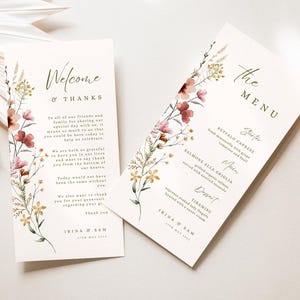 Könnte beinhalten: Zwei Hochzeitskarten mit floralem Design. Die erste Karte lautet "Willkommen & Danke" und enthält eine Dankesbotschaft an die Gäste. Die zweite Karte lautet "Die Speisekarte" und listet die Menüpunkte für den Hochzeitsempfang auf: Buffalo Caprese, Salmone Alla Griglia und Tiramisu.