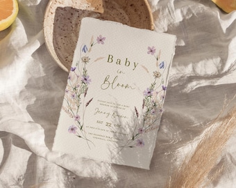 May include: A baby shower invitation with a floral design. The invitation reads "Baby in Bloom" and includes the date and time of the shower. The invitation is printed on a textured paper.