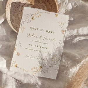 May include: Save the date card with a floral design in shades of beige, yellow, and light purple. The card reads "Save the Date Joshua & Harrah Are Getting Married 01.09.2023 The Barn, at Bidleded, Devon Formal invitation to follow."