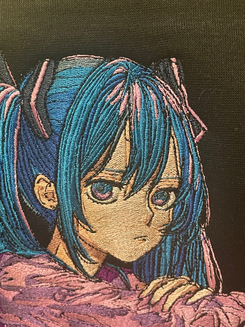 Puede incluir: Imagen bordada de un personaje de anime con cabello azul y ojos morados. El personaje lleva un atuendo rosa y morado y tiene una expresi&oacute;n triste.