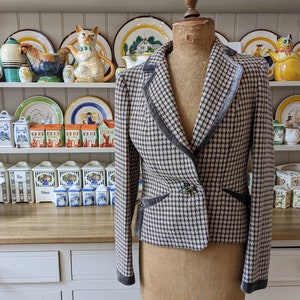 Könnte beinhalten: Ein braunes und weißes kariertes Blazer mit schwarzem Samtbesatz und einem grünen Knopf. Der Blazer befindet sich auf einem Mannequin und wird vor einem weißen Regal mit Dekorationsartikeln ausgestellt.