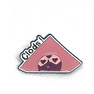 May include: Pink enamel pin with a cartoon character wearing heart-shaped sunglasses. The text "Clods!" is written on the pin.