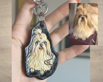 May include: A black leather keychain with a painted image of a white Shih Tzu dog. The keychain has a silver metal ring and a silver metal clasp.