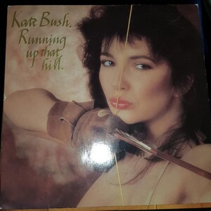 May include: A vintage vinyl record cover featuring Kate Bush. The cover art shows a woman with dark hair holding a bow and arrow. The text on the cover reads "Kate Bush. Running up that hill."