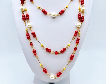 May include: A layered necklace with red and yellow beads and white pearls. The necklace is on a white display stand.