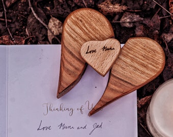 May include: A wooden heart-shaped decoration with a smaller heart that reads "Love Muni" is placed on a card that says "Thinking of You, Love Muni and Jad". A lit candle is in the background. The wooden hearts have a natural wood grain.