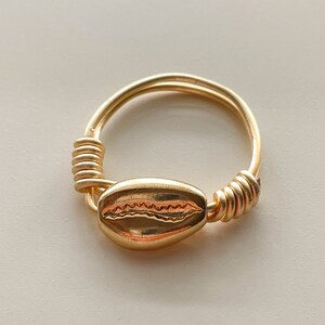 May include: A gold ring with a shell design. The ring is made of twisted wire and has a simple, elegant design.