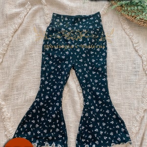May include: Dark teal bell-bottom pants with a white floral pattern. The pants have a high waistband and a flared leg with a scalloped edge. The text "Bellini Bells" and "Nostalgia's Patterns" are visible.