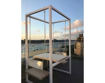 May include: A white swing set with a wooden table and two seats. The swing set is on a rooftop with a view of a city skyline and a body of water.