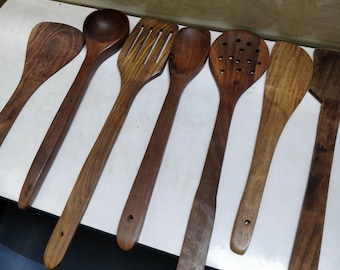 Puede incluir: Conjunto de ocho utensilios de cocina de madera, que incluyen una cuchara, una espátula, una cuchara ranurada y una cuchara de servir. Los utensilios son todos de madera marrón natural y tienen mangos largos.