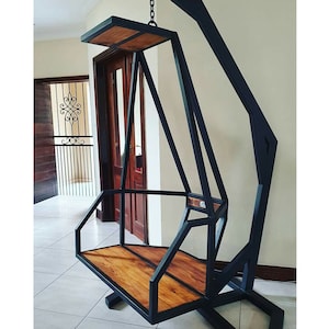 May include: A modern, geometric swing chair with a black metal frame and a wooden seat and canopy. The swing is suspended from a chain and has a unique, angular design. The wooden seat and canopy have a natural wood grain finish.