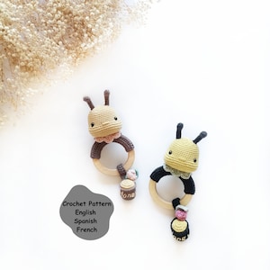 May include: Two crocheted bee rattles with wooden rings. The bees are yellow and brown with black eyes and antennae. Each bee has a small crocheted honey pot attached to the ring.