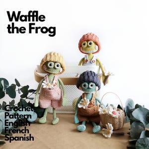 Puede incluir: Tres muñecos de rana tejidos a ganchillo llamados Waffle the Frog, cada uno con un gorro de punto y peto con una pequeña flor. Las ranas son verdes con ojos grandes y mejillas rosadas. Texto Waffle the Frog Crochet Pattern English French Spanish.