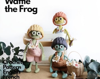 May include: Three crocheted frog dolls named Waffle the Frog, each wearing a knit beanie and overalls with a small flower attached. The frogs are green with large eyes and pink cheeks. Text reads Waffle the Frog Crochet Pattern English French Spanish.