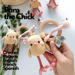Puede incluir: Un juguete de ganchillo con forma de pollito amarillo con mejillas rosas y largas patas rosas unido a un anillo de madera lisa. El pollito tiene alas pequeñas y un mechón de plumas en la cabeza. El texto dice Pam the Chick Crochet Pattern English French Spanish.