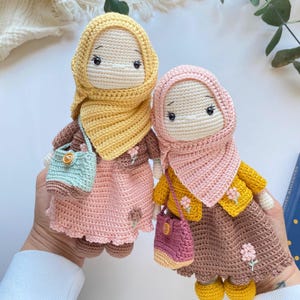 Peut inclure: Deux poupées faites à la main au crochet, chacune portant un hijab et une robe. L'une a un hijab jaune et une robe rose, l'autre a un hijab rose et une robe marron. Les deux poupées ont de petits sacs et des détails de fleurs.