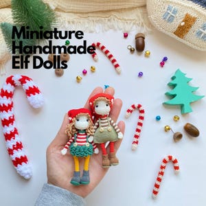 May include: Two miniature handmade elf dolls with crocheted details. One doll wears a red hat, striped shirt, and green skirt with yellow legs. The other wears a red hat, striped shirt, and green overalls. Text reads: Miniature Handmade Elf Dolls.