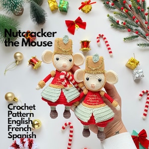 Op de afbeelding: Twee gehaakte muispoppen verkleed als notenkrakers, met beige gezichten, grote oren, gouden hoeden met lichtblauwe accenten, rode jasjes met gouden borduursels en lichtgroene rokjes. De tekst luidt Nutcracker the Mouse Crochet Pattern English French Spanish.