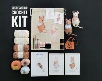 Puede incluir: Un kit de crochet con las palabras "Dudefsworld Crochet Kit" sobre un fondo blanco. El kit incluye hilo, un gancho de crochet, una aguja e instrucciones para hacer un amigurumi de ratón. El kit también incluye una pequeña bolsa con un diseño de ratón y una bolsa con forma de calabaza.