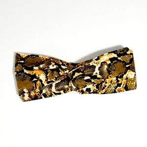 May include: A brown, yellow, and black patterned headband with a twisted knot design.