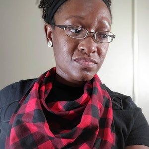 May include: A person wearing a black shirt with a red and black plaid scarf. The scarf is tied in a loose knot around the neck.