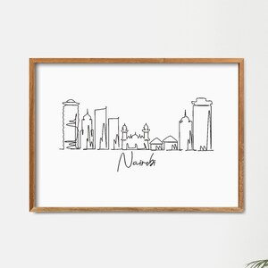 Puede incluir: Una impresi&oacute;n enmarcada que presenta un dibujo lineal minimalista del horizonte de Nairobi. La obra de arte es en negro sobre un fondo blanco, con el nombre de la ciudad debajo. El marco es de madera marr&oacute;n claro.