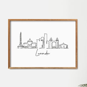 May include: A black and white line drawing of the Luanda skyline, featuring several buildings and a tall monument. The drawing is framed in a light wood frame and is hanging on a white wall. The text "Luanda" is written below the drawing.