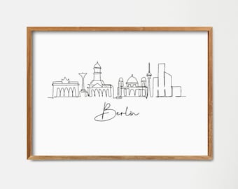 May include: A framed black and white line drawing of the Berlin skyline with the word "Berlin" written underneath. The drawing is on a white background and the frame is a light brown wood.