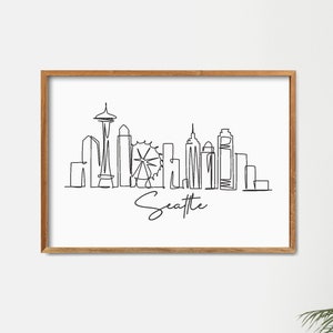 May include: A black and white line drawing of the Seattle skyline, including the Space Needle and the Ferris wheel. The drawing is framed in a light brown wood frame and is hanging on a white wall.